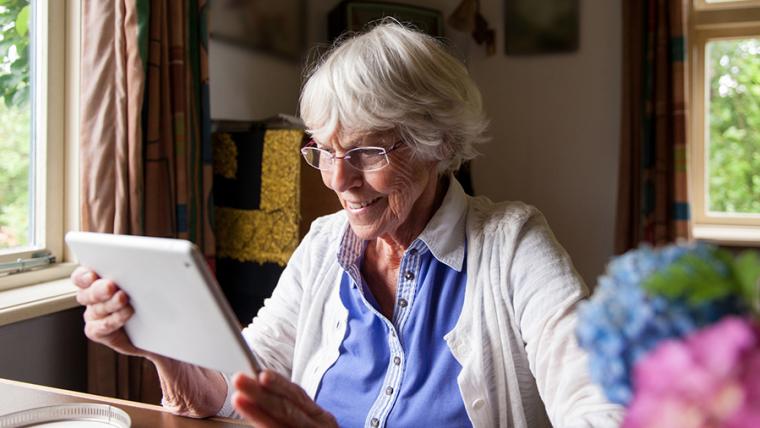 personne âgée souriante sur tablette dans sa maison